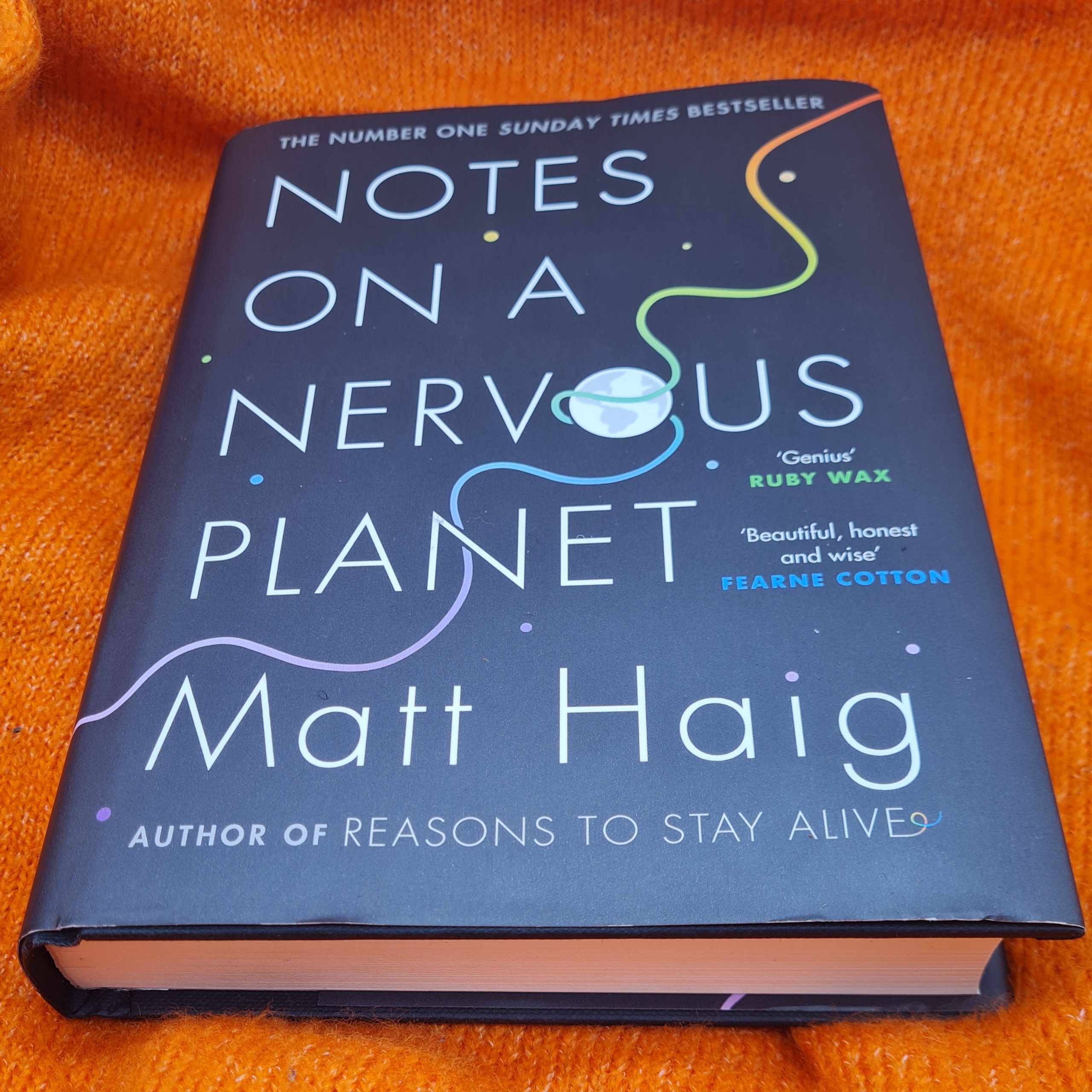 Photo of the book Notes on a Nervous Planet by Matt Haig on an orange background